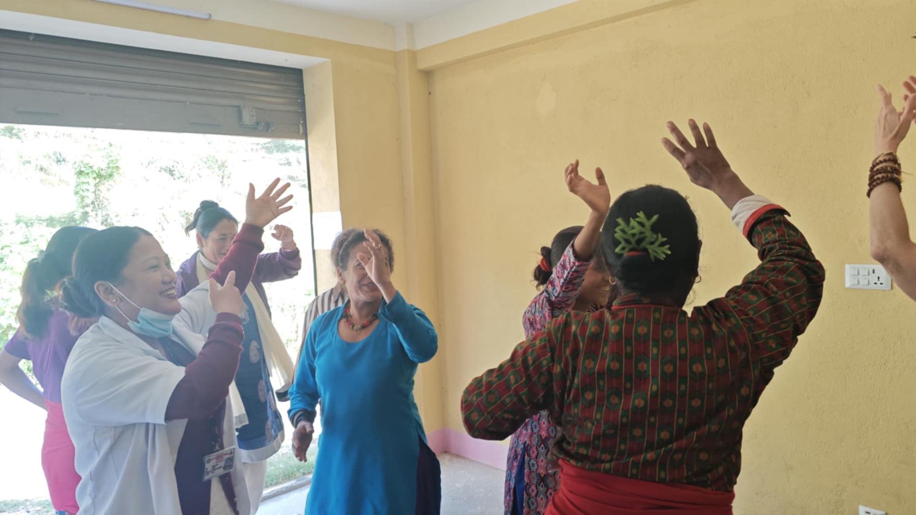 Women in a sunlit room in Nepal dancing with their arms raised