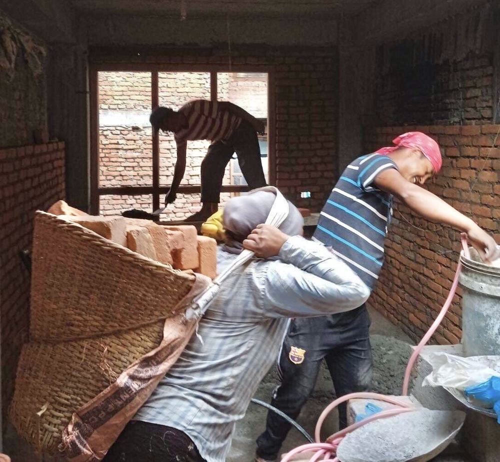 Workers carrying bricks inside a house under construction